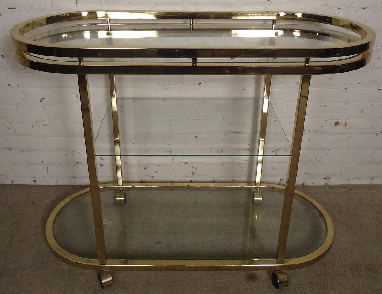Unique solidly built vintage polished brass and glass bar cart designed by Milo Baughman for DIA, Design Institute of America. Set on rolling casters with two oval shelves and a middle glass shelf. Handsome mobile cart for bar ware.

(Please