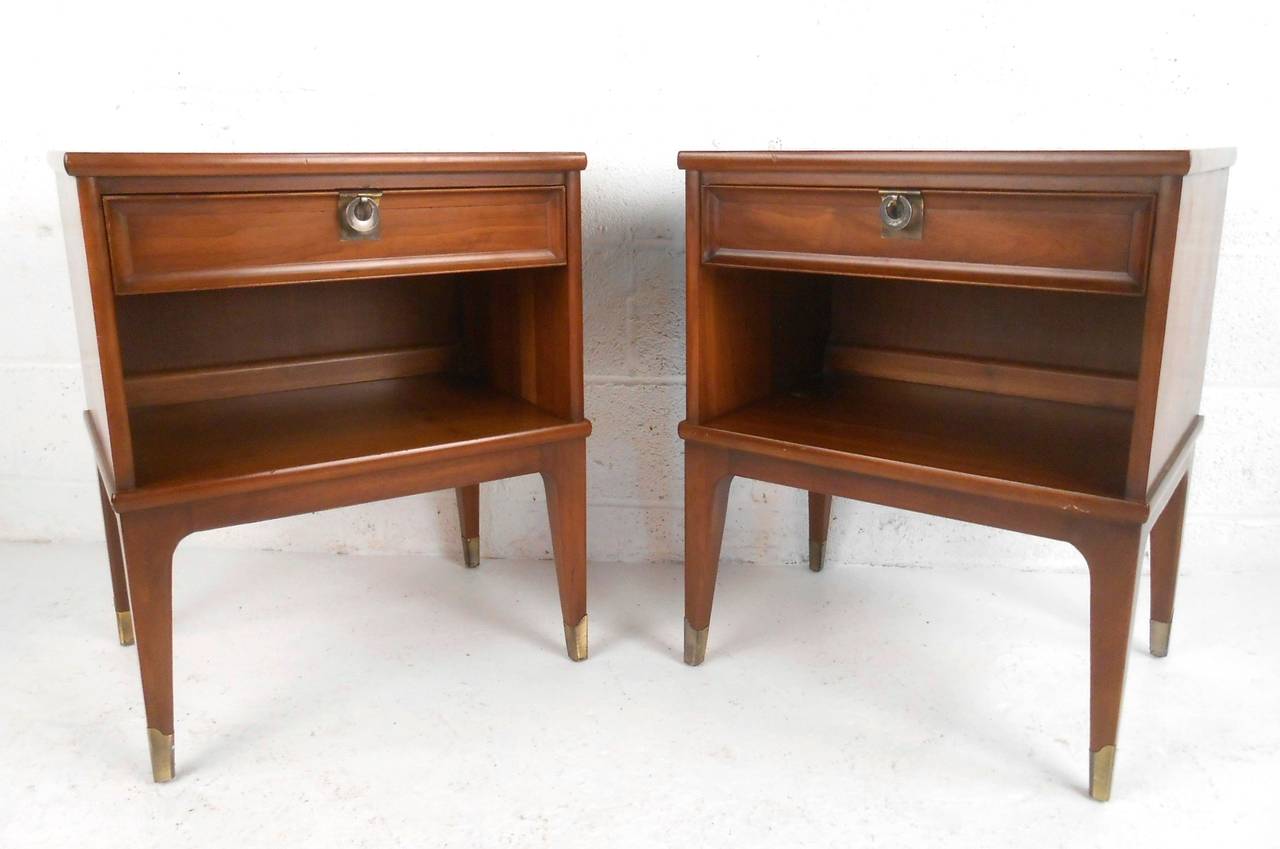 This pair of vintage nightstands feature brass pulls and feet, unique lines and tapered legs. Single drawer and complimentary shelf make this a stylish storage solution in any room. Please confirm item location (NY or NJ).