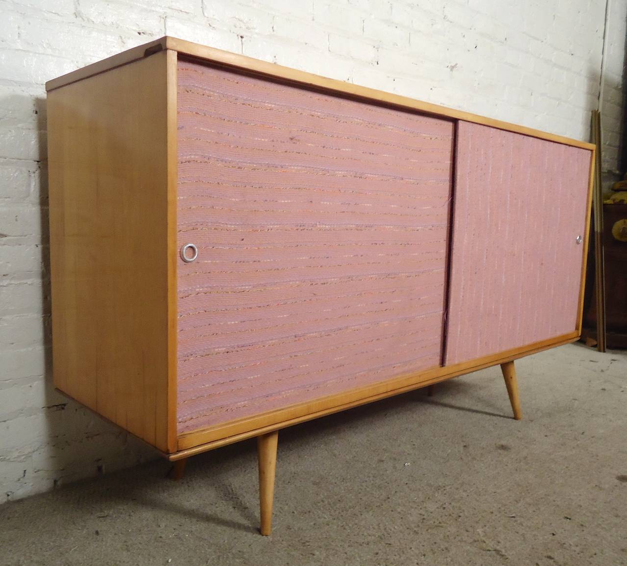Classic credenza designed by Paul McCobb for Winchendon, with sliding grass cloth doors, blonde maple wood and short cone legs. Adjustable shelf on left side. 

(Please confirm item location - NY or NJ - with dealer).
