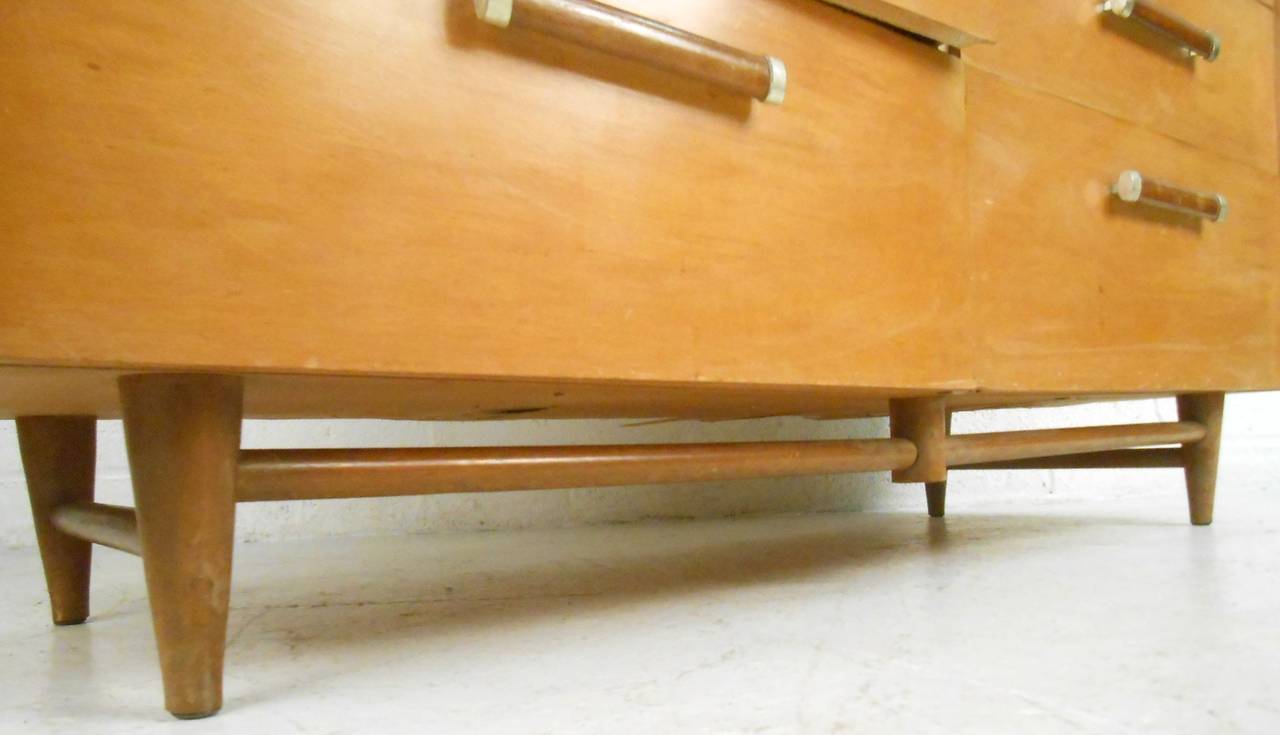 This vintage maple dresser offers stylish storage in a uniquely mid-century fashion. Tapered legs are reinforced with stretchers while unique drawer pulls feature brass trim. Matching highboy dresser also available, please confirm item location (NY