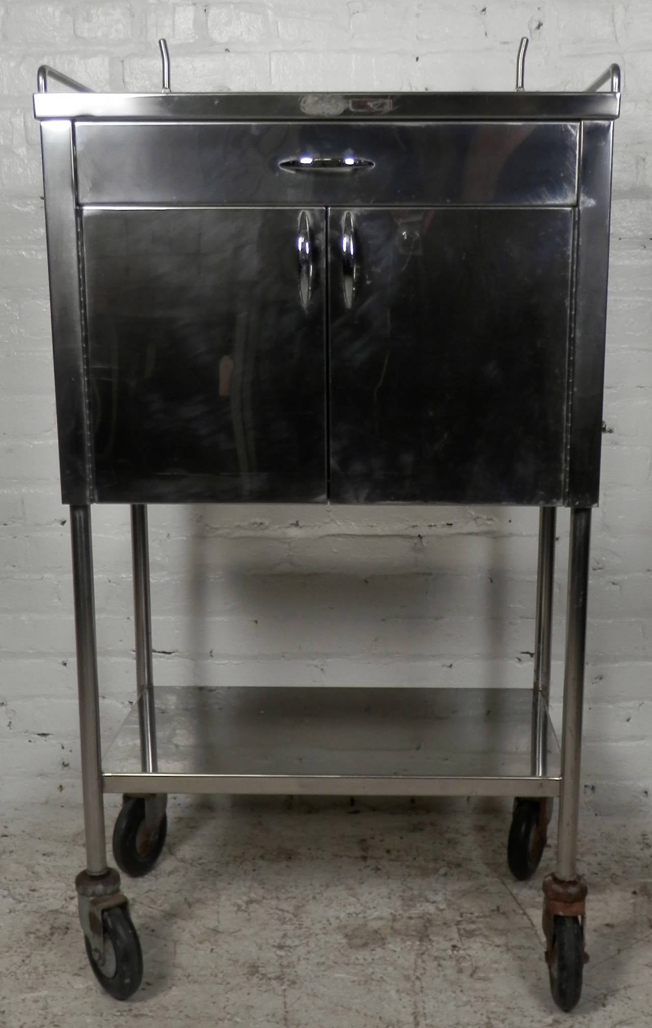 Polished stainless steel medical cart on wheels featuring one drawer and a two door cabinet revealing one metal shelf inside. Makes a great addition to your modern bathroom.

(Please confirm item location - NY or NJ - with dealer)