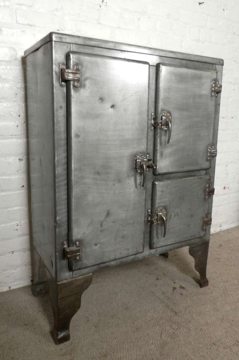 A great storage unit for home or office. 
Three door cabinet with removable wood shelves. Features original latches, curved feet, refinished in a bare metal finish giving a great machine age style.
Makes a great dry bar!

(Please confirm item