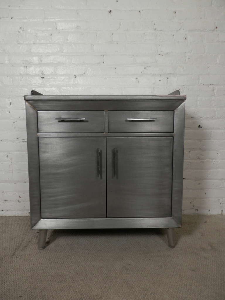 Industrial metal doctors cabinet from the first half of the 20th Century, refinished in a brush metal style. Laminate top, drawers and a two door cabinet. Features original curved metal handles and cone shape legs.

Great for bathroom or kitchen