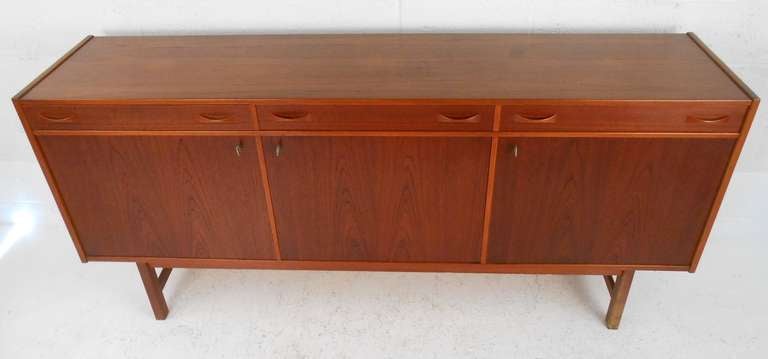 Long and narrow teak server by Ulferts of Tibro, Sweden. Three dove-tailed drawers with one divided over three locking doors containing adjustable shelves. Rich reddish teak finish, uniquely Danish design, and oversized storage cabinets make this a