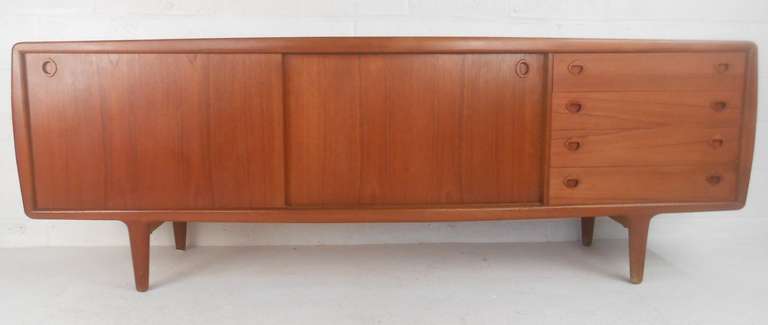 Scandinavian Modern sideboard with Danish teak finish, recessed pulls, tapered legs, and plenty of storage. Unique sculpted trim adds to the vintage modern appeal of this well-crafted server, making it an impressive Mid-Century Modern storage piece