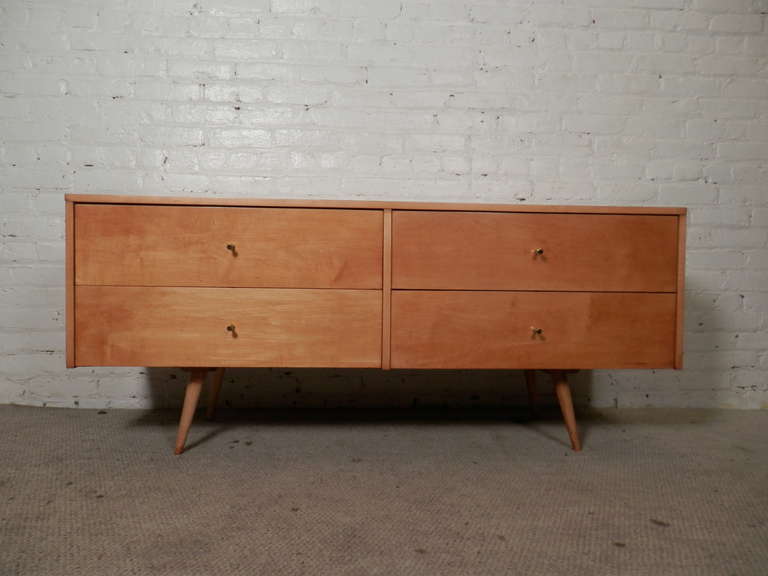 Maple four drawer low console by popular mid-century designer Paul McCobb. Made for his Planner Group series this unit has all the classic McCobb stamps - golden maple grain, cone legs, brass golf tee pulls and clean modern lines. This has been