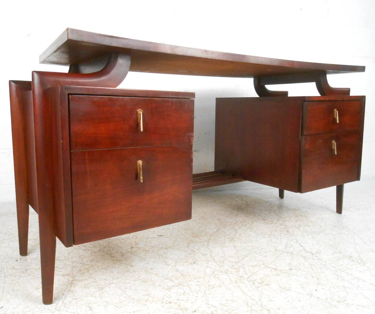 This mid-century desk features a unique shape and Hooker style sculpted floating top. Unique drawer pulls, tapered legs, and a matching desk chair make this a wonderful addition to any home or office. Manufactured by Tri-Bond, please confirm item