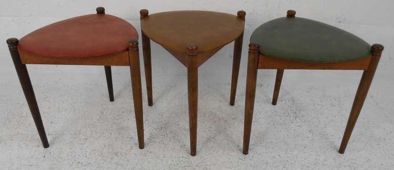Set of three midcentury nesting tables with vinyl tops and tapered legs. This beautiful set sits comfortably on top of one another providing convenient storage. Sleek and functional designs with wonderfully colored seats. Please confirm item