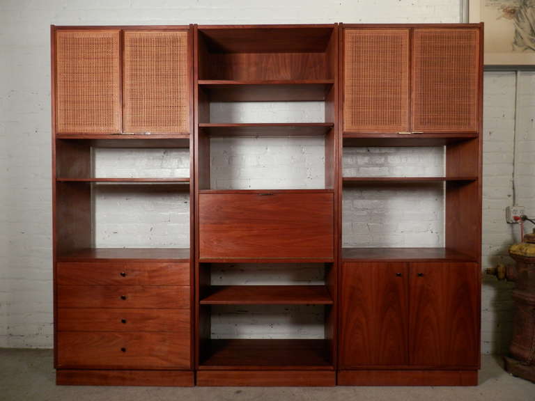 Large mid-century modern modular unit made of three tall standing components. Designed by Founders, made of quality walnut grain with cane front doors, drop front cabinet/desk, drawers and various size cubbies. Makes an immense bookcase or can be