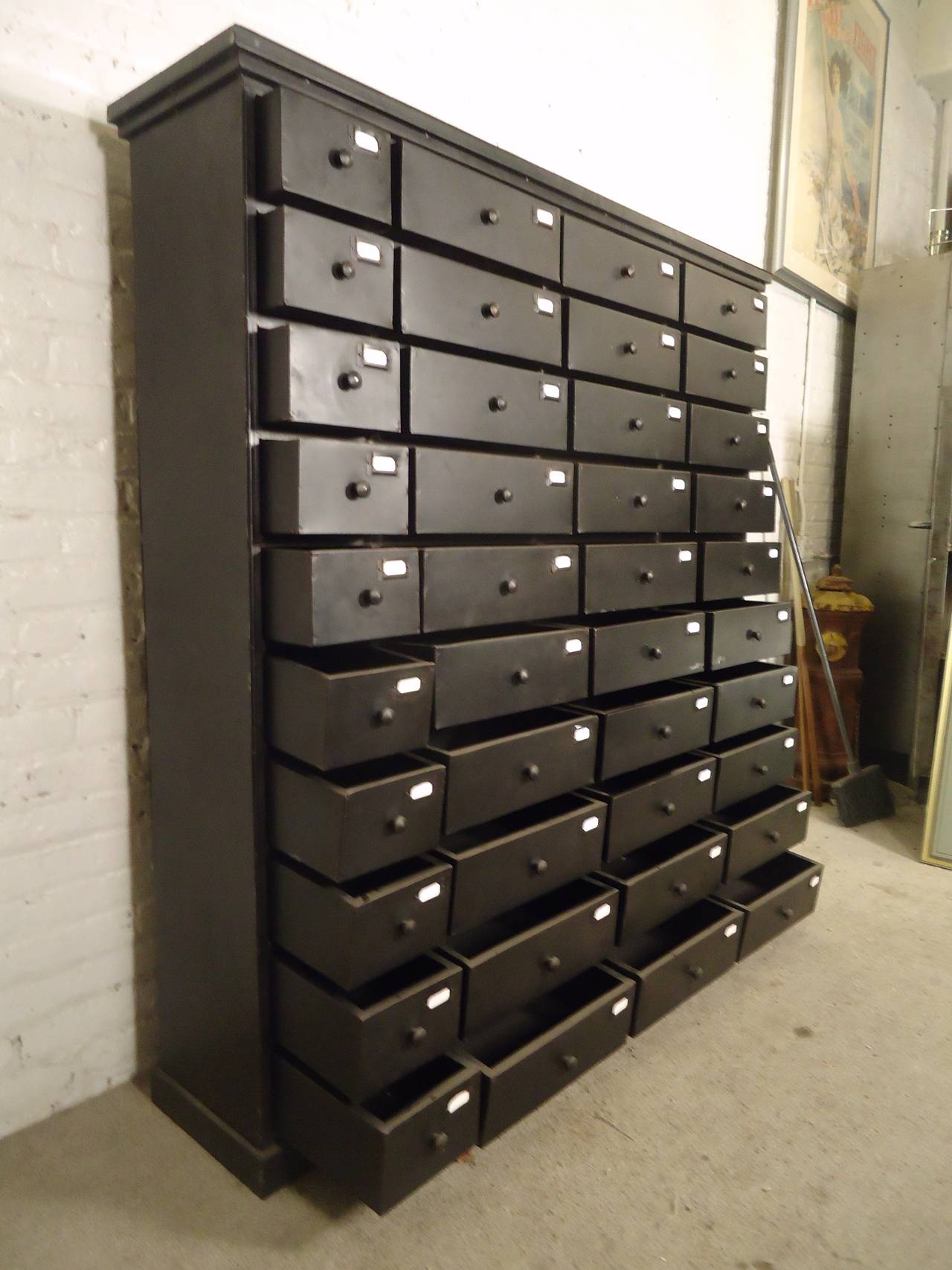 This large-scale industrial modern file cabinet features metal construction with forty drawers of varying size, all with label holders. Great for retail, office, or home display and storage, the unique vintage industrial style makes great room or