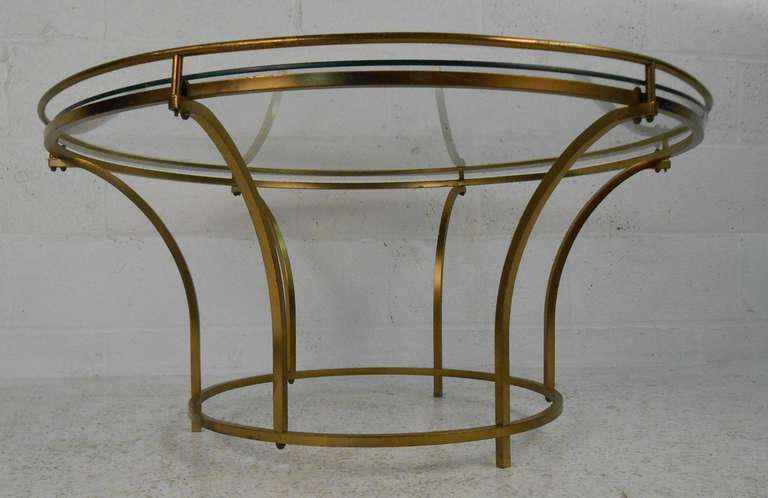 Brass-plated metal frame table with clear glass top. This stylish vintage modern cocktail table boasts curved supports holding up a circular glass top. The sturdy construction and sleek shape makes this table the perfect addition to any modern