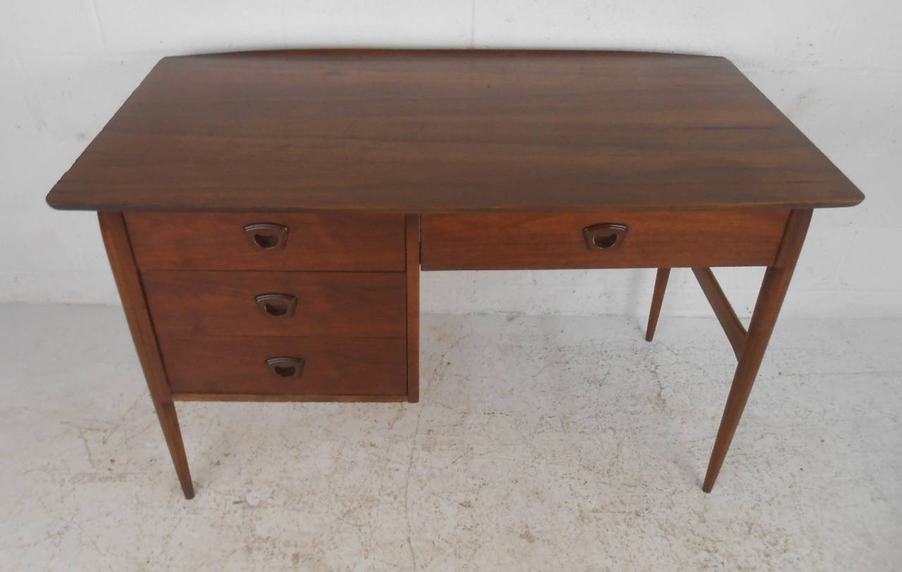 This single pedestal three drawer desk by Bassett Furniture Co makes a stylish vintage modern addition to any home or business office. Unique tapered legs and cutaway drawer handles add to the midcentury appeal of the piece. A well made American
