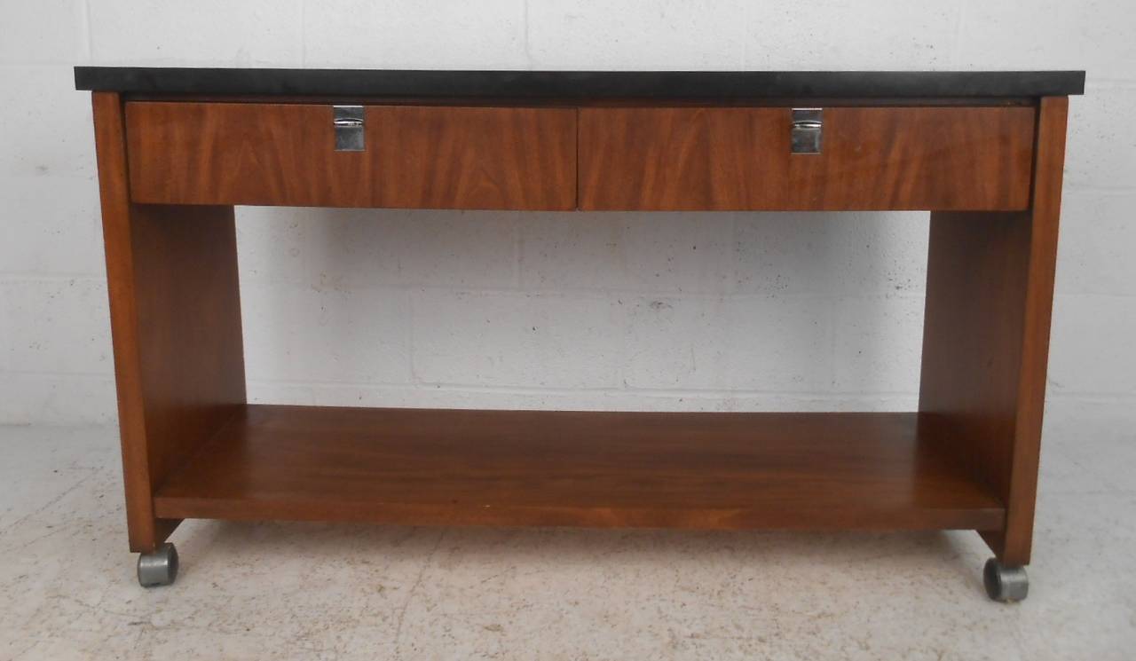 This vintage modern sideboard features walnut finish, black formica style top and casters for versatility and easy service. Excellent console table for dinner service or use as a bar cart. This versatile piece looks great behind the sofa, in the