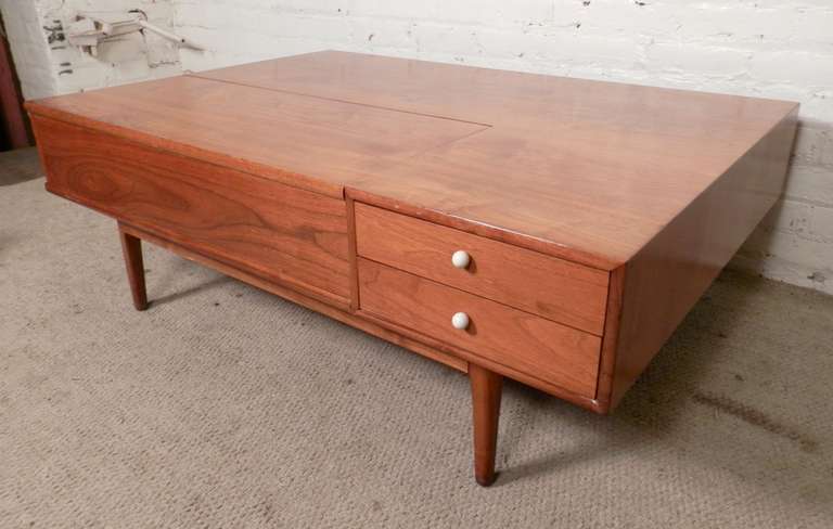 Multifunctional coffee table in warm walnut grain. Features a wide flat surface, flip top lid, small side drawers and open back compartments for plenty of storage. Unusual design features a double sided form.

(Please confirm item location - NY or
