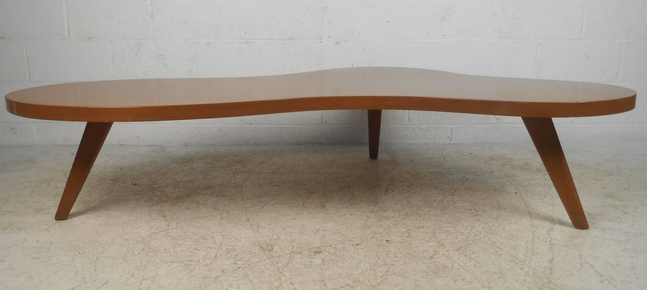 This impressive atomic modern coffee table features sculptural free-edge table top and unique midcentury style attributed to T. H. Robsjohn-Gibbings for Widdicomb. A sleek design with a free form top, splayed legs, and a vintage walnut finish adding