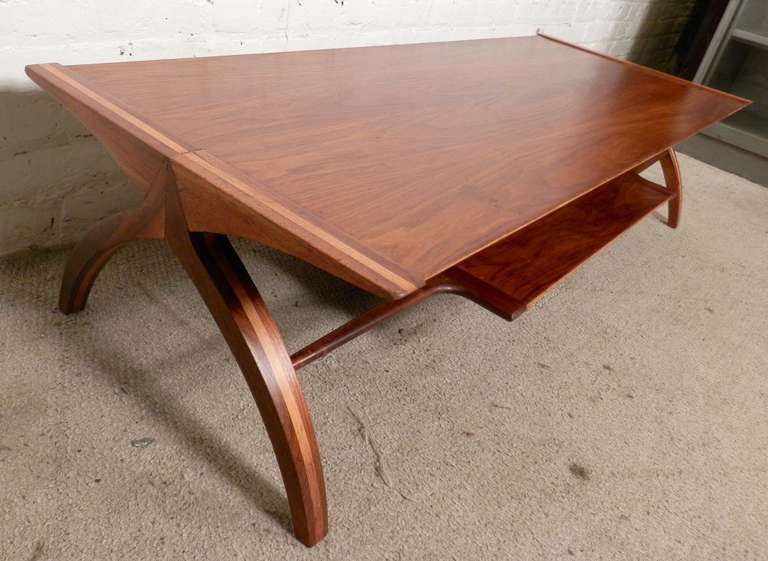 Rare vintage modern coffee table with arched legs, having accenting walnut and blonde oak, delicately sculpted shelf for extra storage, and a rich walnut grain top. Very unusual design with a dramatic flair!

(Please confirm item location - NY or