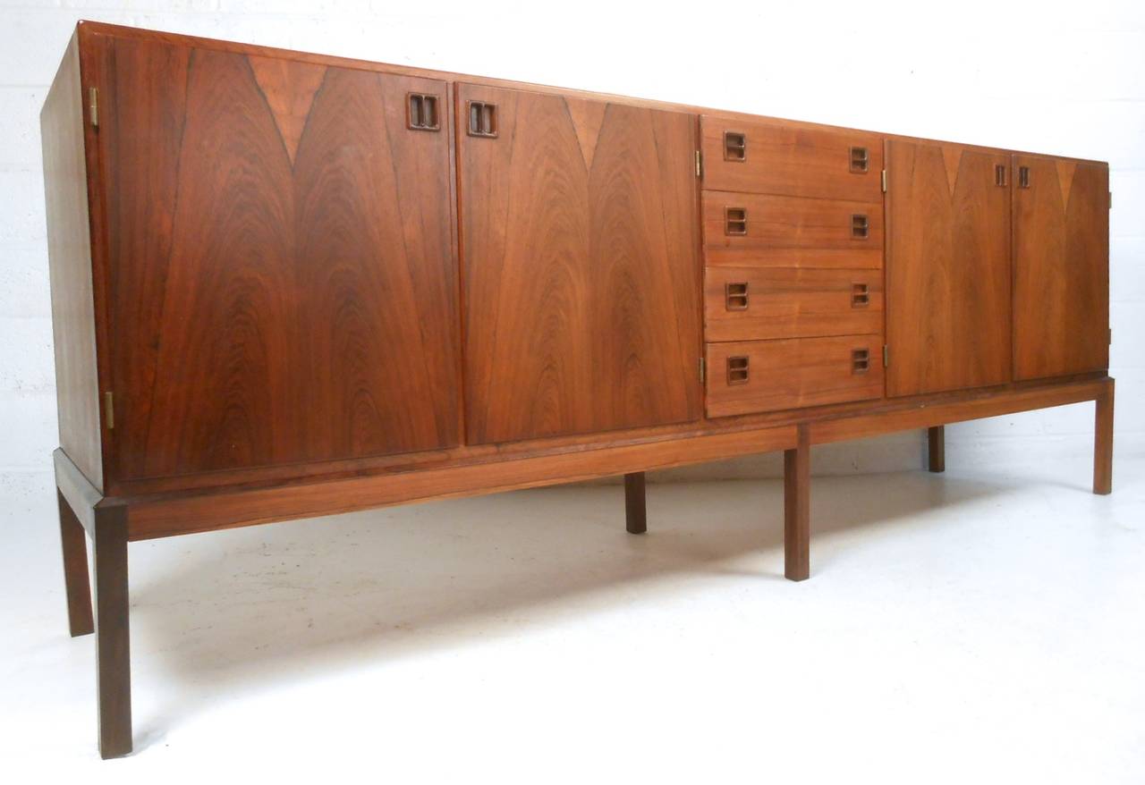 This long vintage sideboard features exquisite rosewood finish, plenty of space for storage, and a wonderful midcentury style. Perfect lines, unique pulls, and added center legs for stability make this piece the perfect addition to any room. Please