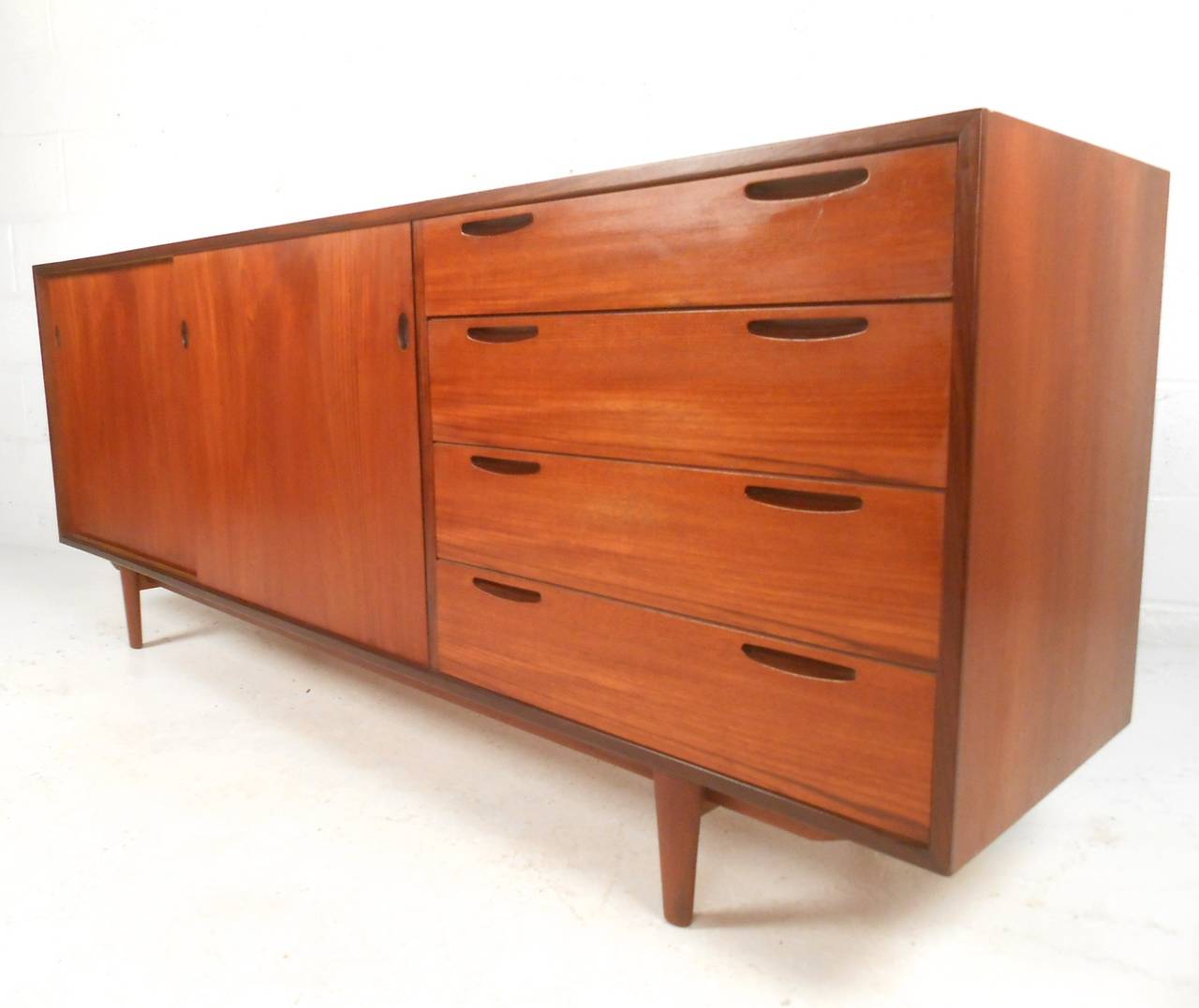 This beautifully crafted mid-century teak credenza is stylish and practical, combining vintage design with natural teak finish to create a truly wonderful addition to any room. Unique drawer pulls, tapered legs, and finished back add to the