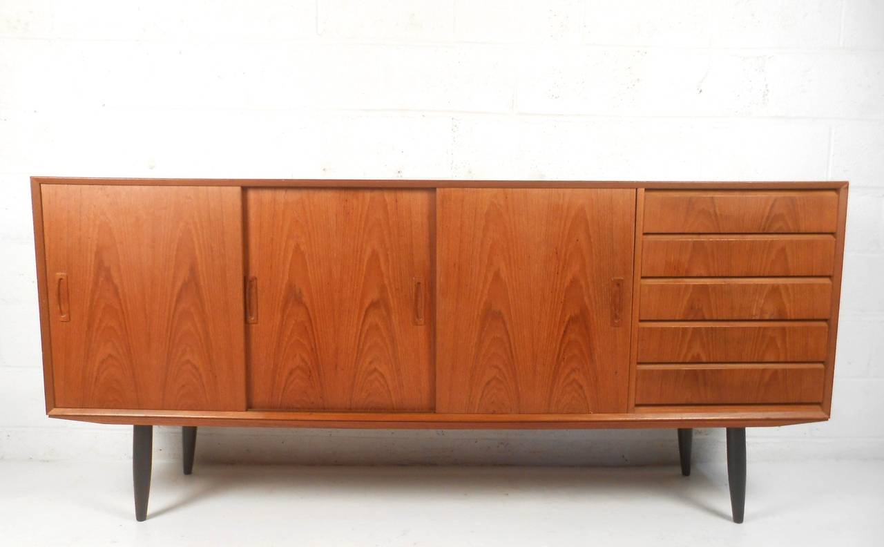 This unique vintage sideboard combines sliding door cabinet storage with a set of five drawers to accommodate storage needs of any size. Unique tapered legs, dovetail construction, and fabulous teak finish make this a wonderful addition to any