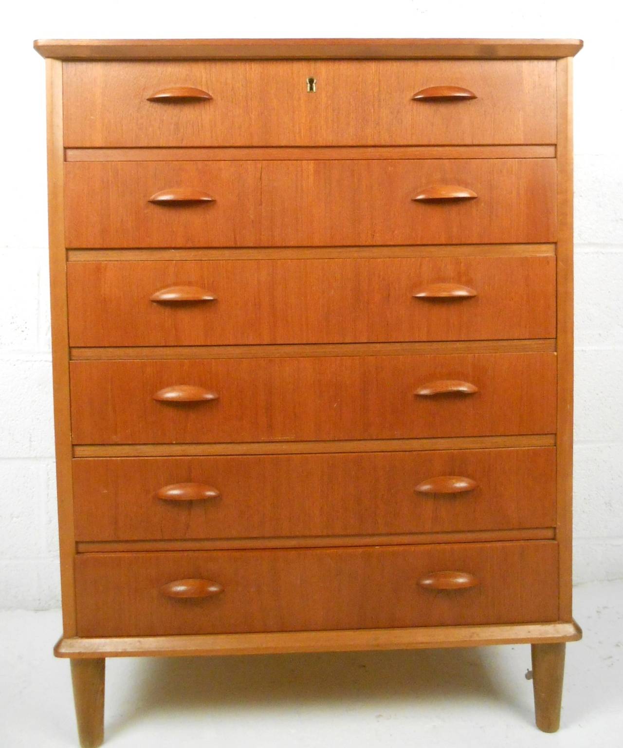 This unique mid-century dresser features a lovely teak finish, uniquely carved drawer pulls, and six spacious drawers for storage. Please confirm item location (NY or NJ).