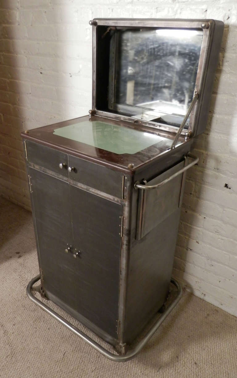 This is a fantastic find! 
Deco era metal barber station with flip top mirror and light, drawers and cabinet space and 360 degree casters. Newly restored with a bare metal finish to accommodate the modern home decor. Great as a rolling