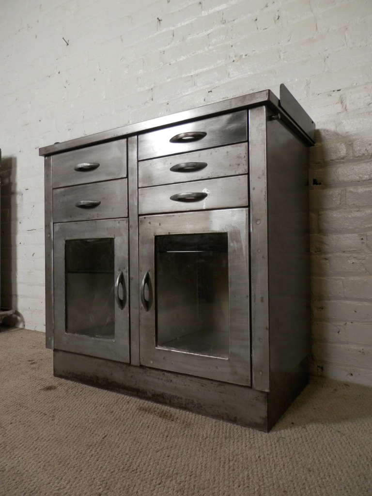 Heavy duty industrial cabinet from the early 20th Century, newly restored to a bare metal finish for home use in the kitchen or bathroom. Features multiple pull out drawers, glass cabinet doors and removable supply rack.

(Please confirm item
