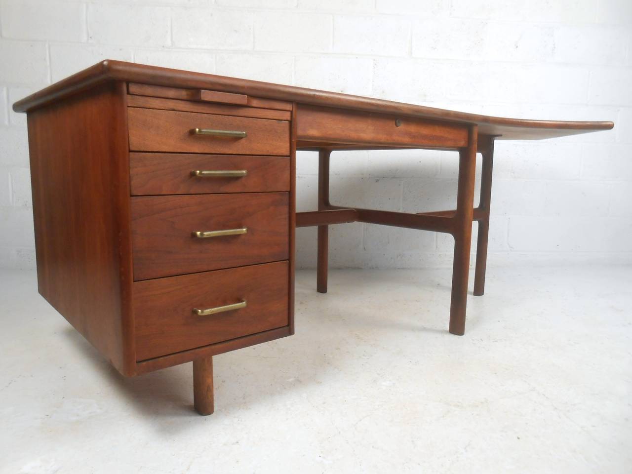 This imposing vintage desk features sturdy walnut construction, brass drawer pulls, and heavy duty metal drawer glides. Plenty of work space for any office, the uniquely shaped desk top adds to it's versatility and style. Please confirm item