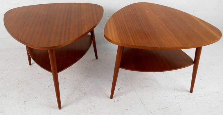 A stunning pair of mid-century modern side tables with a guitar pick shaped top. This sleek pair boasts a two-tier design with tapered legs and beautiful wood grain throughout. A functional and stylish pair of end tables that make the perfect