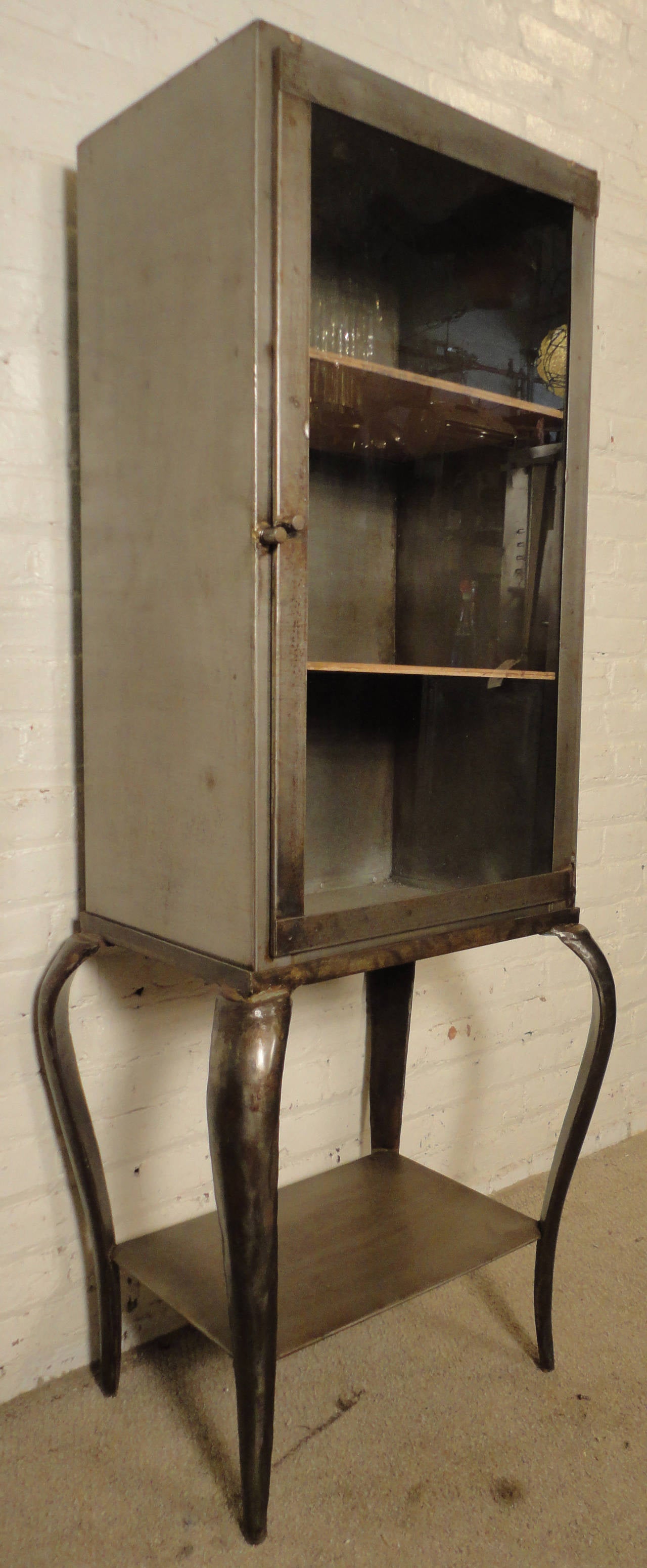 Industrial display cabinet, features latching glass door, two wooden shelves, beautifully sculpted legs and lower storage.

(Please confirm item location - NY or NJ - with dealer)