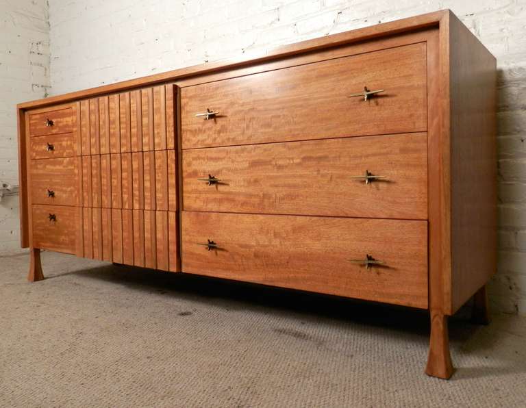 Fantastic Mid-Century design with sculpted front, polished mahogany grain and ten dovetailed drawers, made by John Widdicomb. Stylish all around, with the main stand out being the original brass 