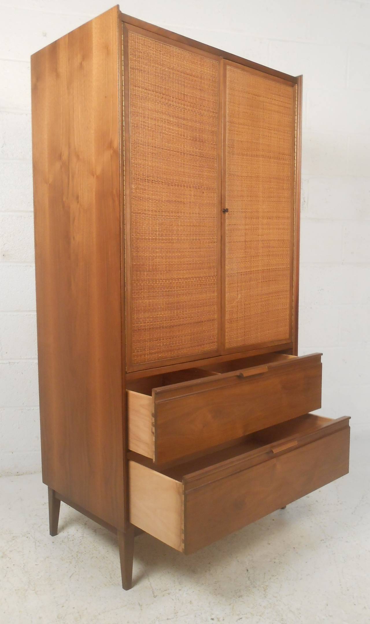 Attractive walnut mid century cabinet with cane front doors revealing four pull-out storage trays and three cubbies on top and two large drawers at bottom. Please confirm item location (NY or NJ) with dealer.
