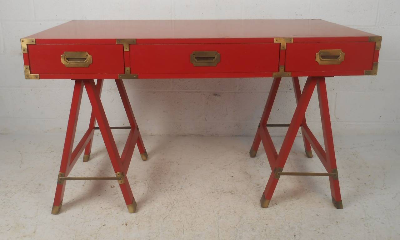 Three-drawer campaign desk in red finish with bass trim, folding sawhorse legs and matching chair. Ideal workspace or writing desk for home or business office. Please confirm item location (NY or NJ) with dealer.