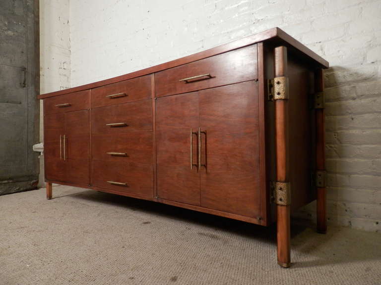 Long impressive dresser/sideboard by Romweber with a curved bow tie shape body, textured brass hardware, twelve drawers and a heavy, sturdy frame. A newly finished walnut grain exterior helps the hand hammered brackets and handles pop out with great
