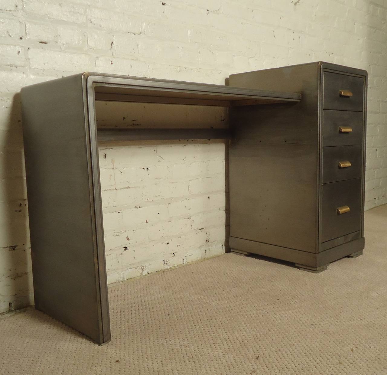 Vintage deco style desk with unusual tiered top designed for Simmons by Norman Bel Geddes. Newly restored in a bare metal style finish with complimenting original brass handles. Open desk space with ample storage.
Kneehole dimensions: 33