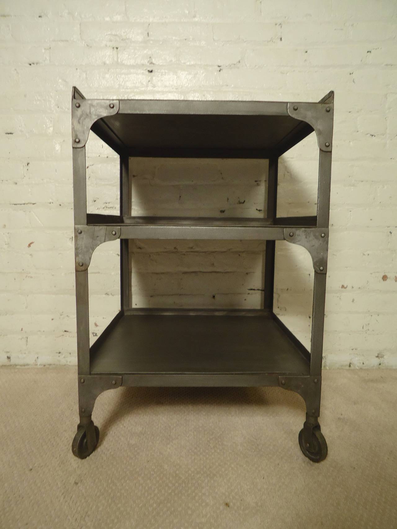 Metal shelving unit on casters restored in a bare metal style finish. Handsome industrial look with exposed rivets. Makes for attractive storage in your modern living room or bathroom.

(Please confirm item location - NY or NJ - with dealer)