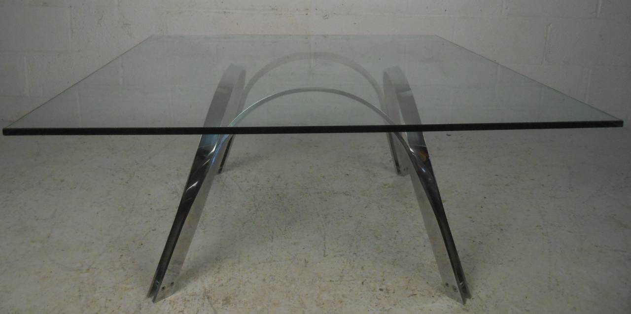 Nice vintage glass top coffee table in the style of Roger Sprunger for Dunbar. This sleek midcentury cocktail table boasts arched sides, splayed legs, and a large glass top. The heavy sculpted chrome base is sure to make a lasting impression in any