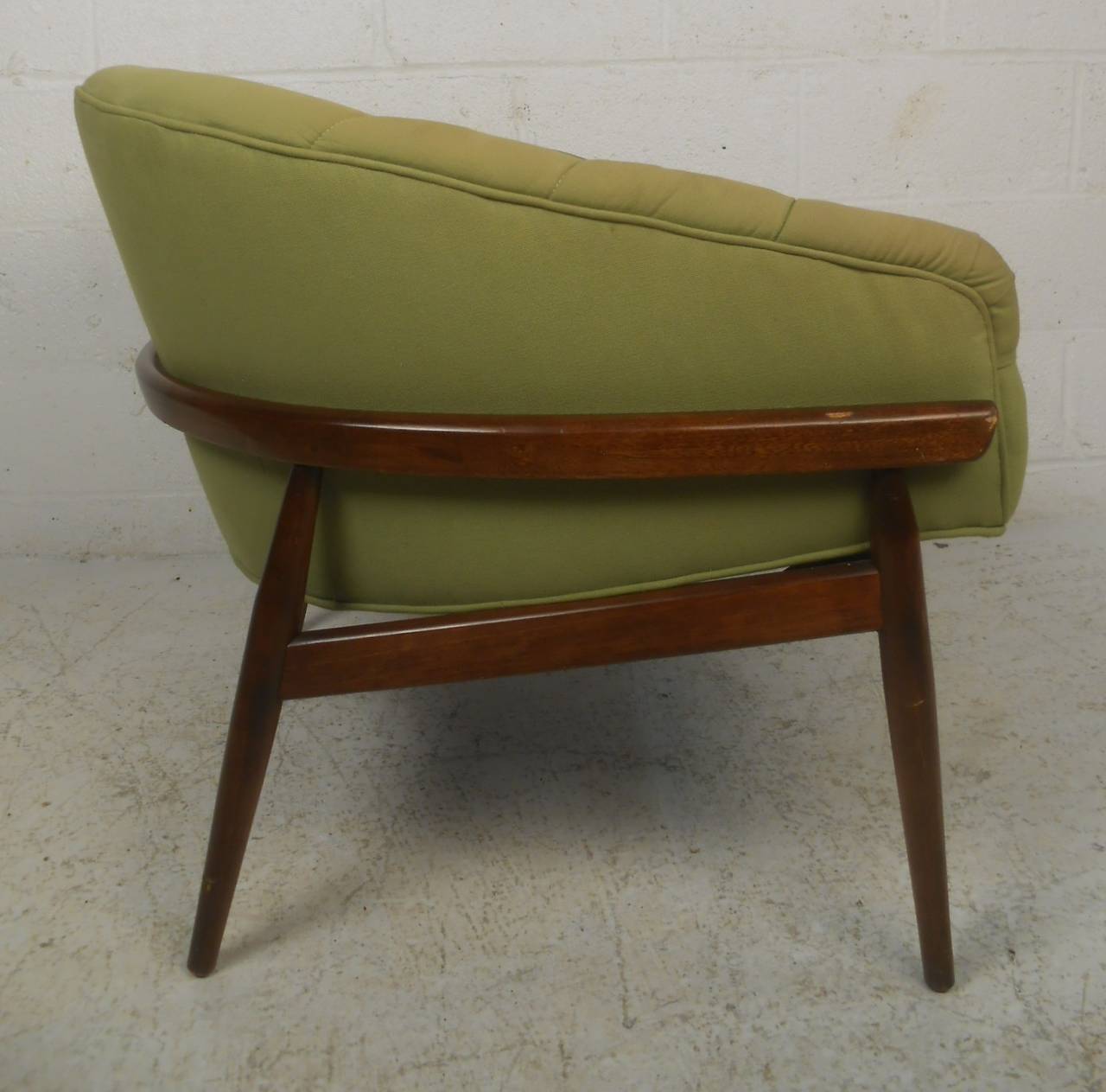 Mid-Century Modern walnut frame lounge chair with barrel back rest and tufted green upholstery. A wide design with overstuffed seating ensuring maximum comfort. Quality craftsmanship that boasts a sculpted dark walnut frame with tapered and splayed