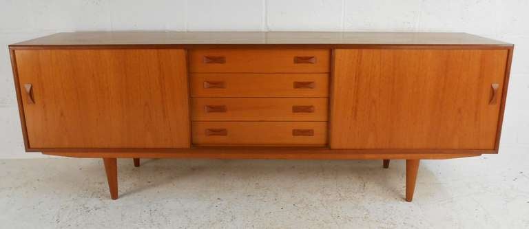 Teak sliding door sideboard with adjustable shelves and four centre drawers makes a striking storage piece for dining room or living room. Rich mid-century teak wood finish with spacious interior shelved storage. Please confirm item location (NY or