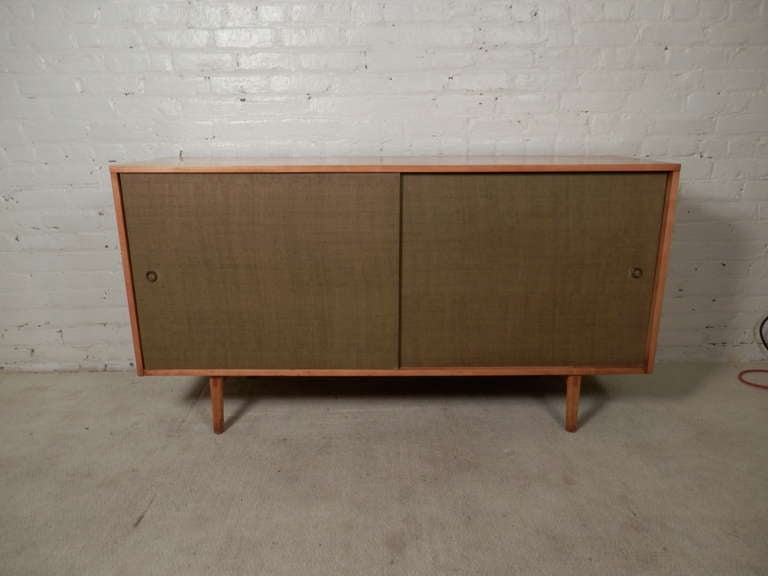 Fantastic maple credenza with lite green grass cloth sliding doors. Designed by Paul McCobb for the Planner Group line. A classic mid-century modern look. Clean lines, two open cabinets with four total drawers, and tapered legs.

(Please confirm