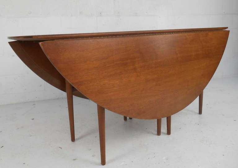 This mid-century modern drop leaf table is constructed of solid American walnut and features a unique oval shape accented by brass hardware. Unusual for an oval shape in mid-century tables, similar to the Dunbar made table by Edward