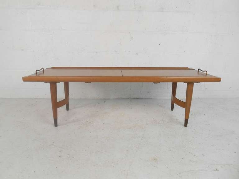 This midcentury American coffee table features an expandable sliding top, unique curved wood stretcher and brass pulls and feet. Please confirm item location (NY or NJ) with dealer.