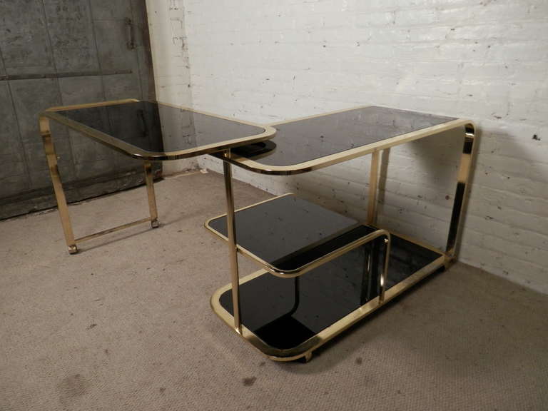 Vintage modern brass rolling cart with smoked glass. Attributed to designer Milo Baughman, this cart features his classic rounded mid-century design. The black smoked glass accents the gold frame wonderfully. Can be locked in place to move or