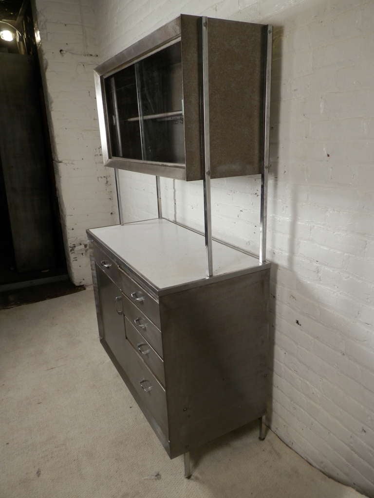 Unusual industrial cabinet which includes five drawers and single door cabinet in the base. The top, which is removable has a sliding glass open cabinet with shelf. Very unique for an early 20th century style metal cabinet.

(Please confirm item