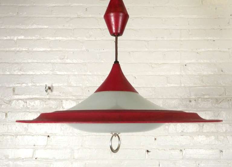 Esta impresionante lámpara colgante vintage de mediados de siglo presenta una llamativa pantalla de metal rojo esmaltado combinada con un difusor de cristal opaco, que evoca el diseño elegante y futurista de un platillo volante o la caprichosa forma