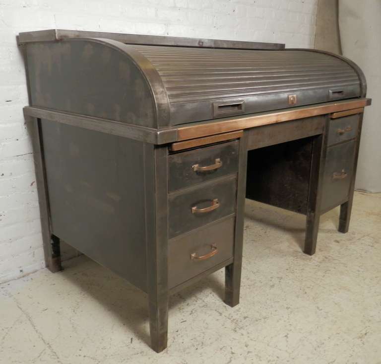 Heavy industrial metal desk with functional roll top. Opens to an original green rubber flat desk top with multiple compartments. Brass hardware highlights the masculine striped metal finish. A hard to find, one of a kind!

(Please confirm item