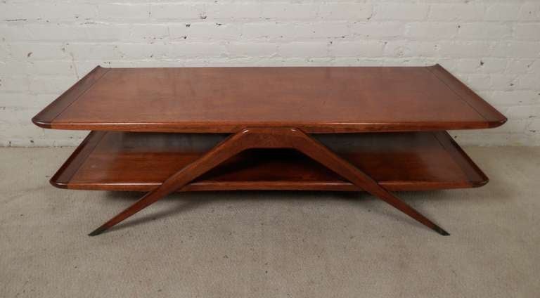 Unique vintage modern coffee table with two shelves, both with curved edges giving an elegant look. Angled v-shape legs with brass feet. A very different styled table.

(Please confirm item location - NY or NJ - with dealer)
