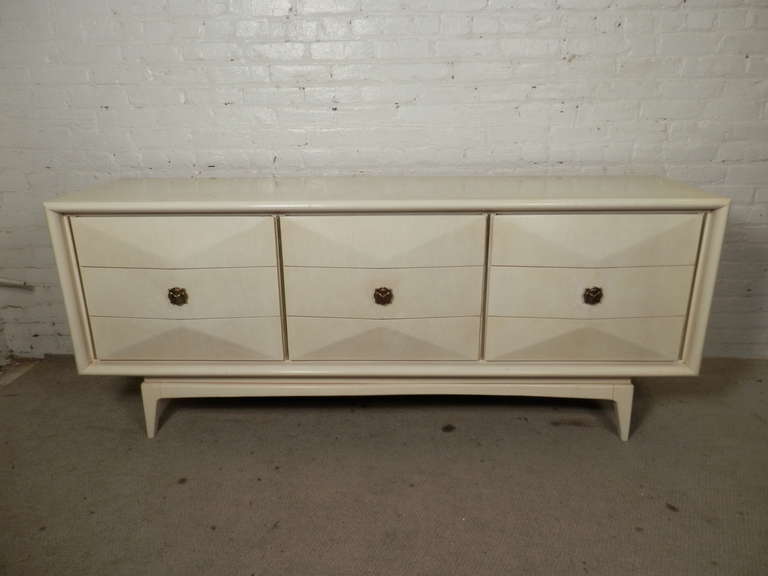 This mid-century modern nine drawer dresser was manufactured by United Furniture Corporation and features a sculpted diamond front, beautiful white lacquer finish, Hollywood Regency style brass pulls and sits on tapered legs. 

Please confirm item