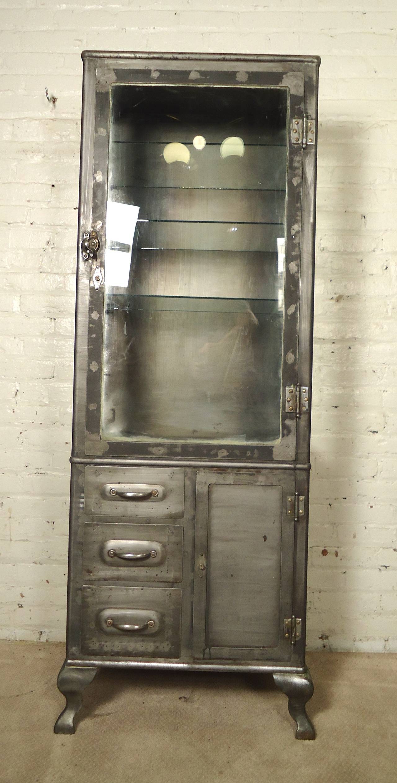 Attractive Industrial metal display cabinet, refinished in a bare metal style. Three side glass cabinet with removable glass shelves. Additional bottom storage and cabriole legs.
Top cabinet: 23