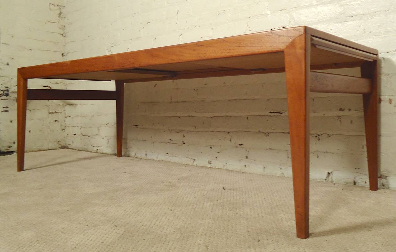 Mid-Century Modern teak table with extending leaves. In addition to the great modern style, tapered legs and teak grain, the draw leaf feature allows for additional table space. One leaf is teak, the other is black laminate. Extends to