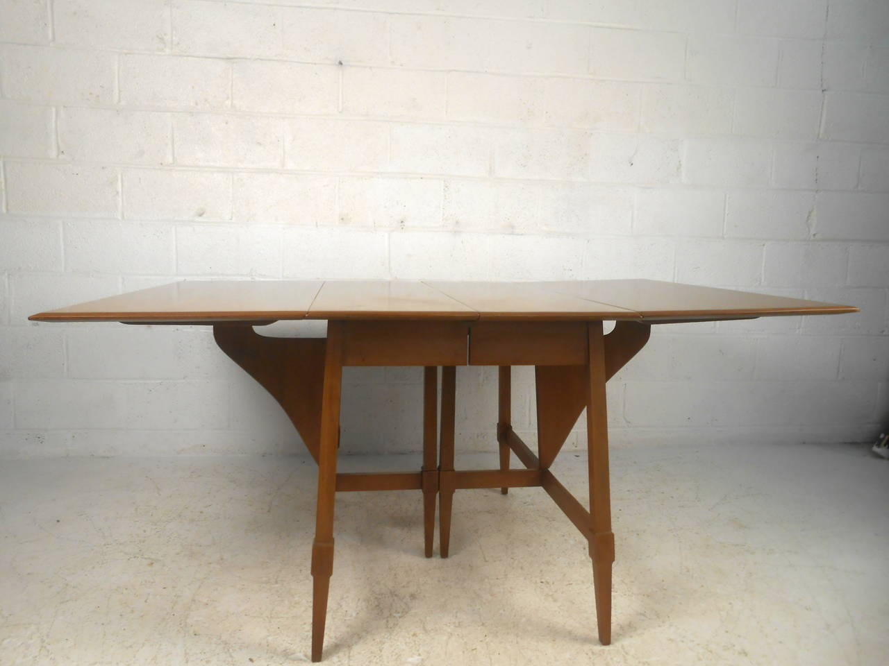 This midcentury dining table features a drop leaf construction, two additional leaves, and unique tapered legs which offer expandable surface and a modern flare to any home or office space. 

Please confirm item location (NY or NJ) with dealer.